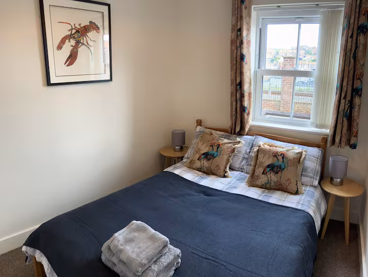 Bedroom with navy bedspread, heron-print cushions and a framed lobster print above the bed.