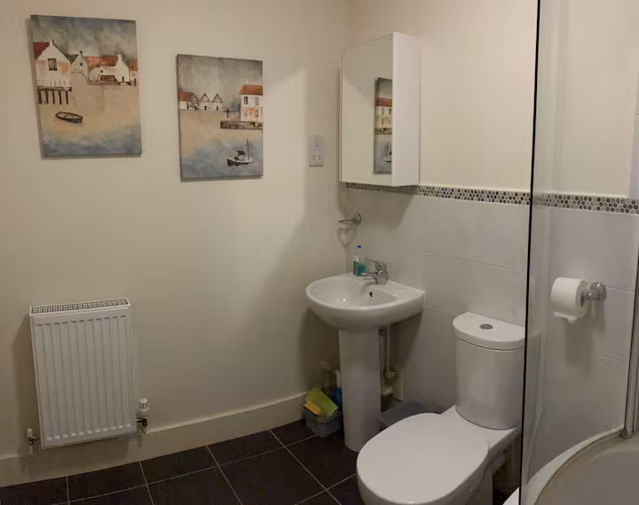 Bathroom with white suite, dark tiled floor and framed harbour-village prints.