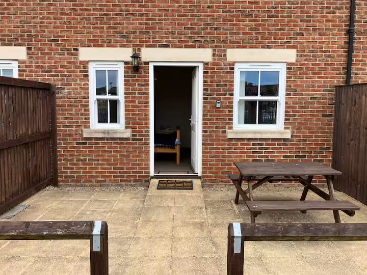Red-brick exterior with private paved courtyard, wooden picnic table and open front door.